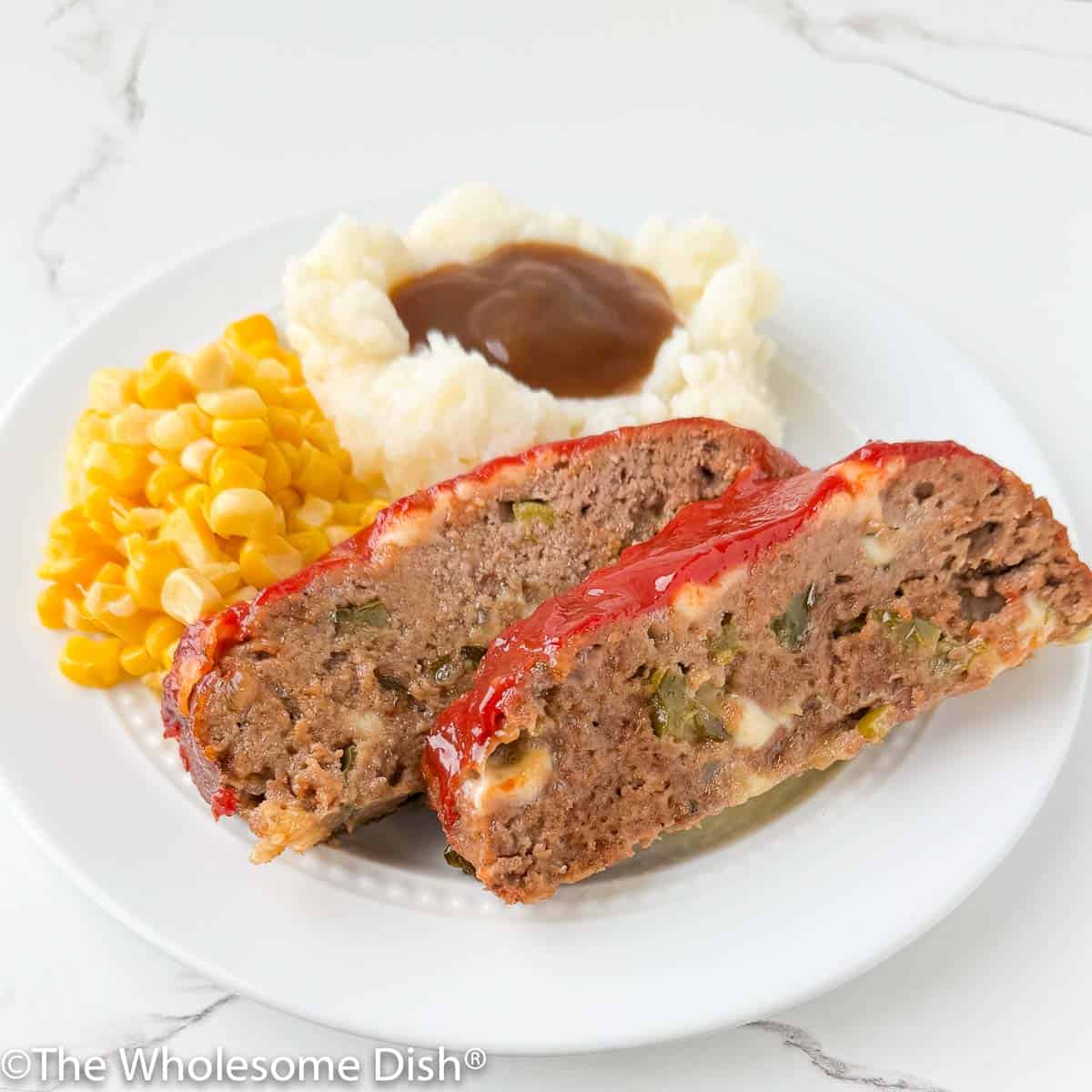 Two slices of meatloaf on a plate with mashed potatoes, gravy, and corn.