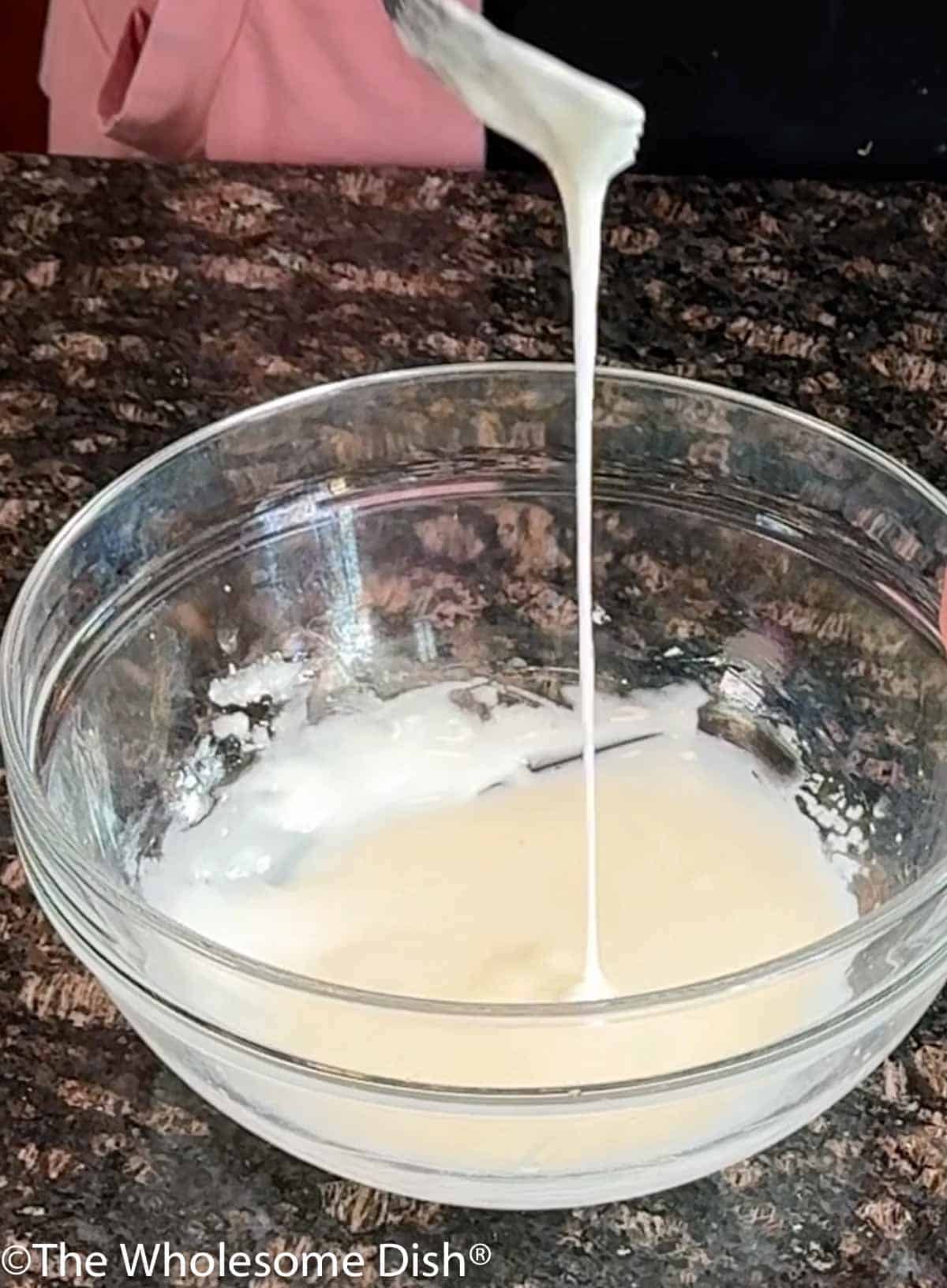 Mixing powdered sugar and lemon juice together in a glass mixing bowl.