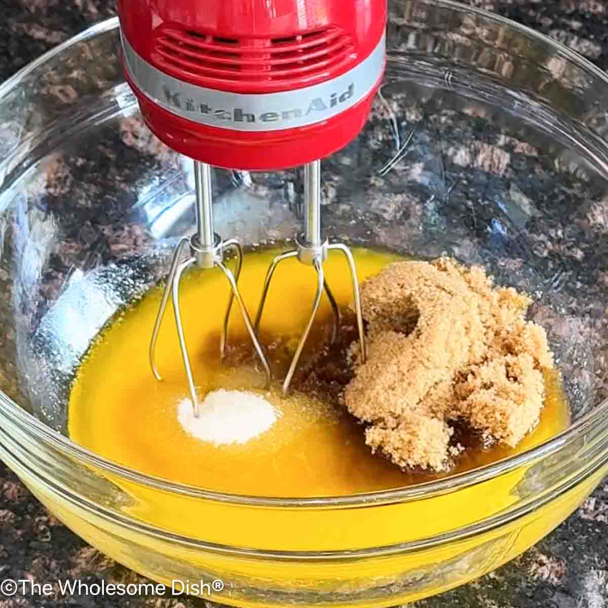 Mixing melted butter, brown sugar, and sugar in a glass mixing bowl.