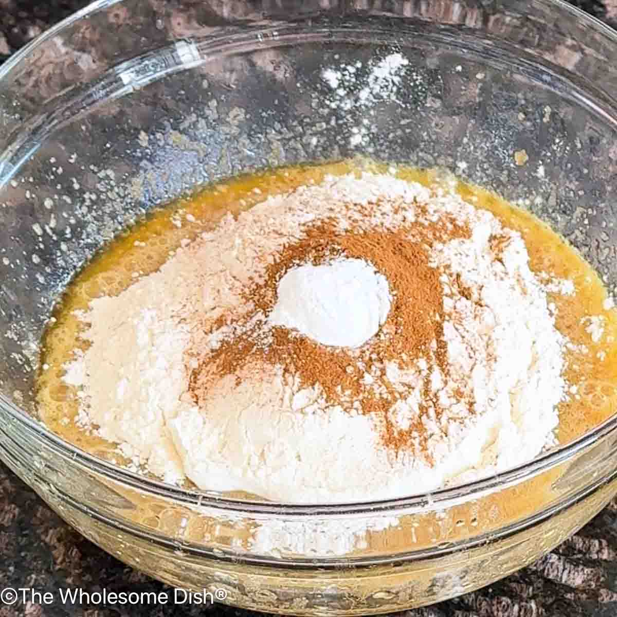 Adding flour, cinnamon, baking powder, and salt to the bowl.