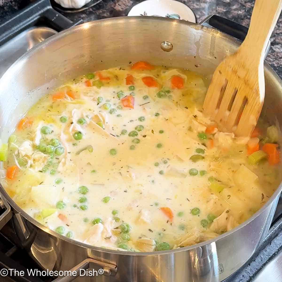 Adding shredded rotisserie chicken, half & half, and frozen peas to the soup pot.