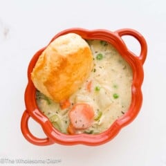 Chicken pot pie soup and a biscuit served in an orange bowl.