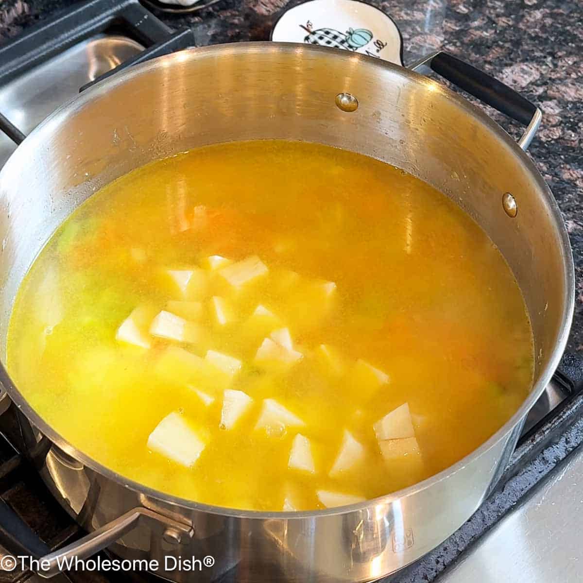 Adding chicken broth and chopped potatoes to the pot.