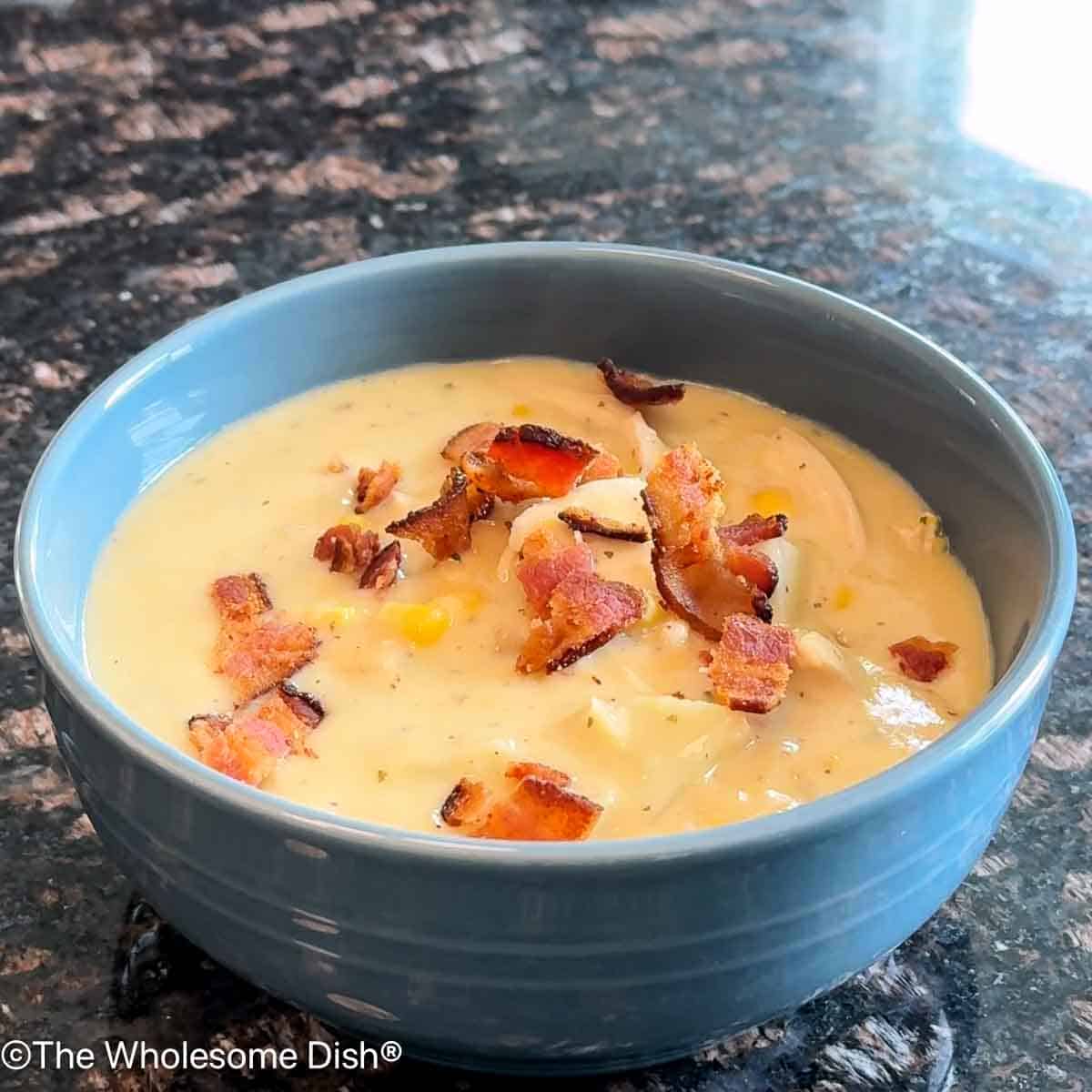 Blue bowl filled with Crack Corn Chowder topped with crumbled bacon.