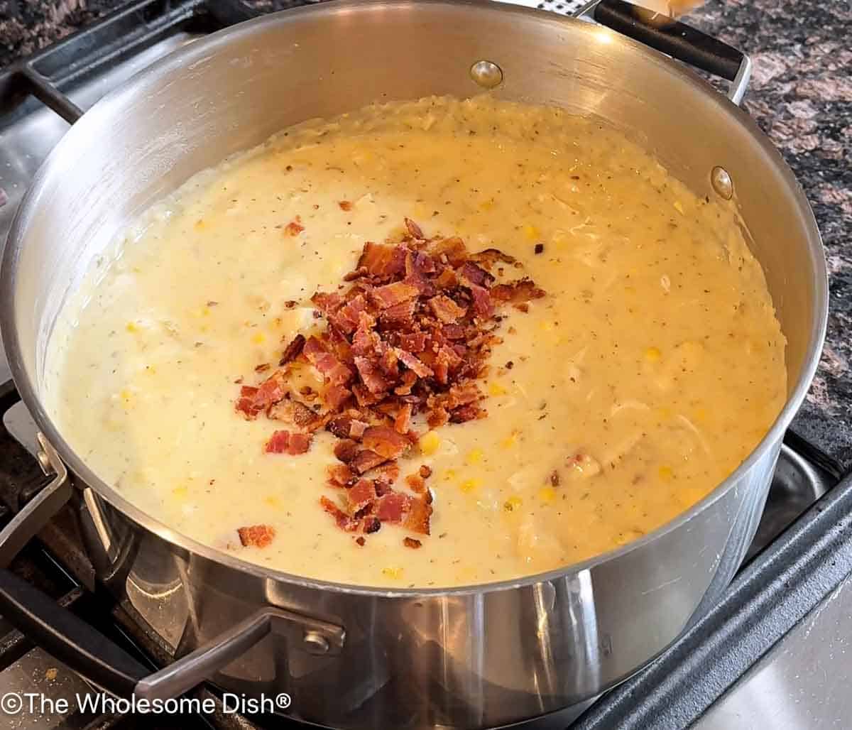 Adding crumbled bacon to the corn chowder.