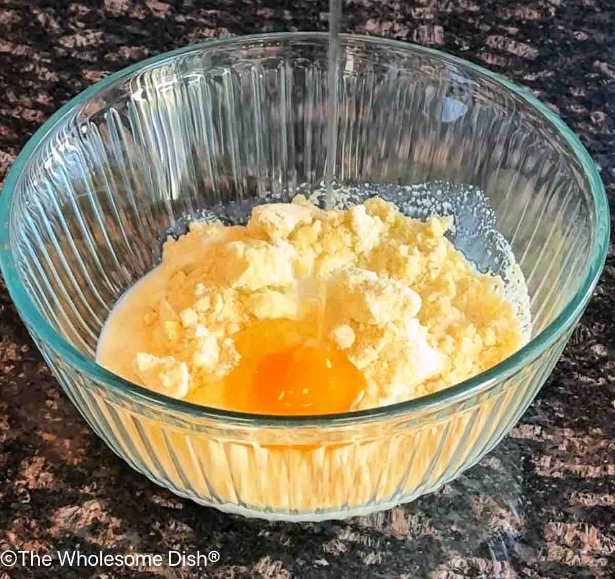 Preparing a box of corn muffin mix in a glass mixing bowl.