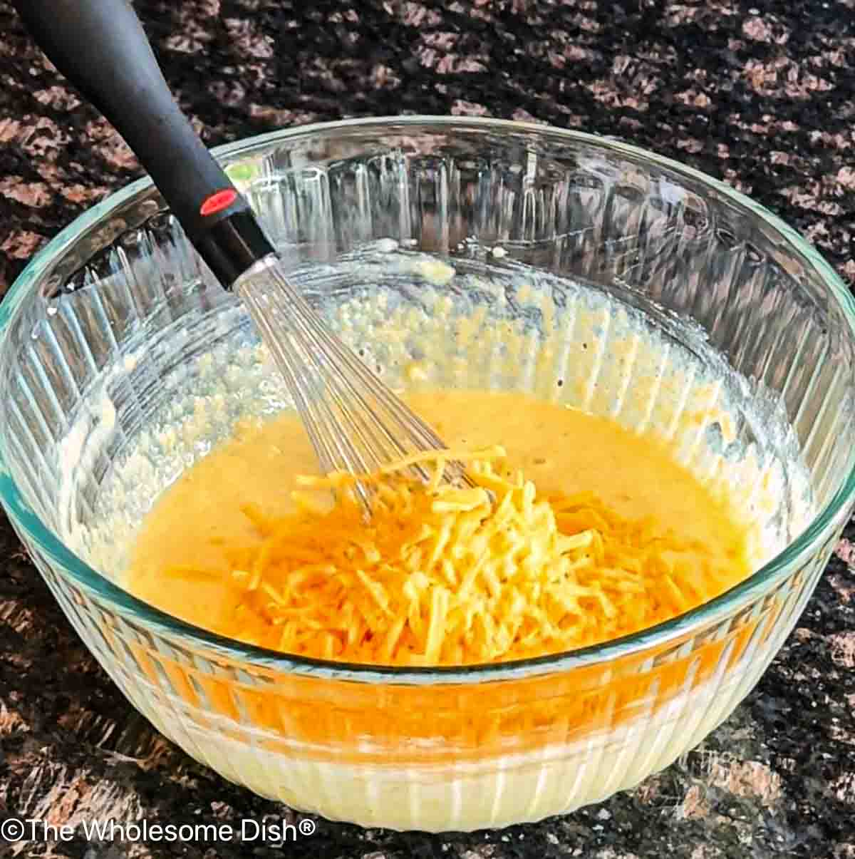 Adding shredded cheddar cheese to the cornbread batter.