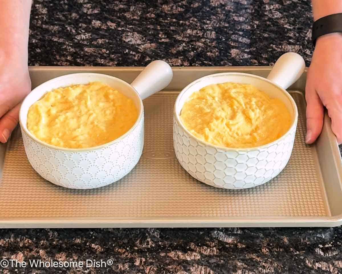 Two bowls filled with soup topped with cornbread batter on a baking sheet.