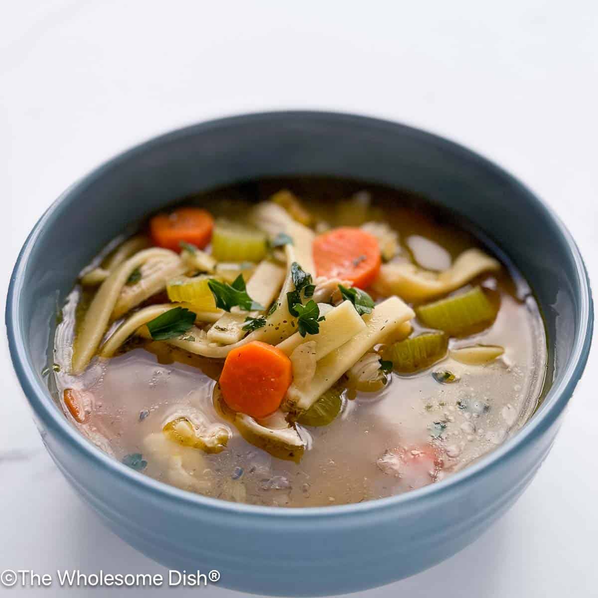 Blue bowl full of chicken noodle soup.