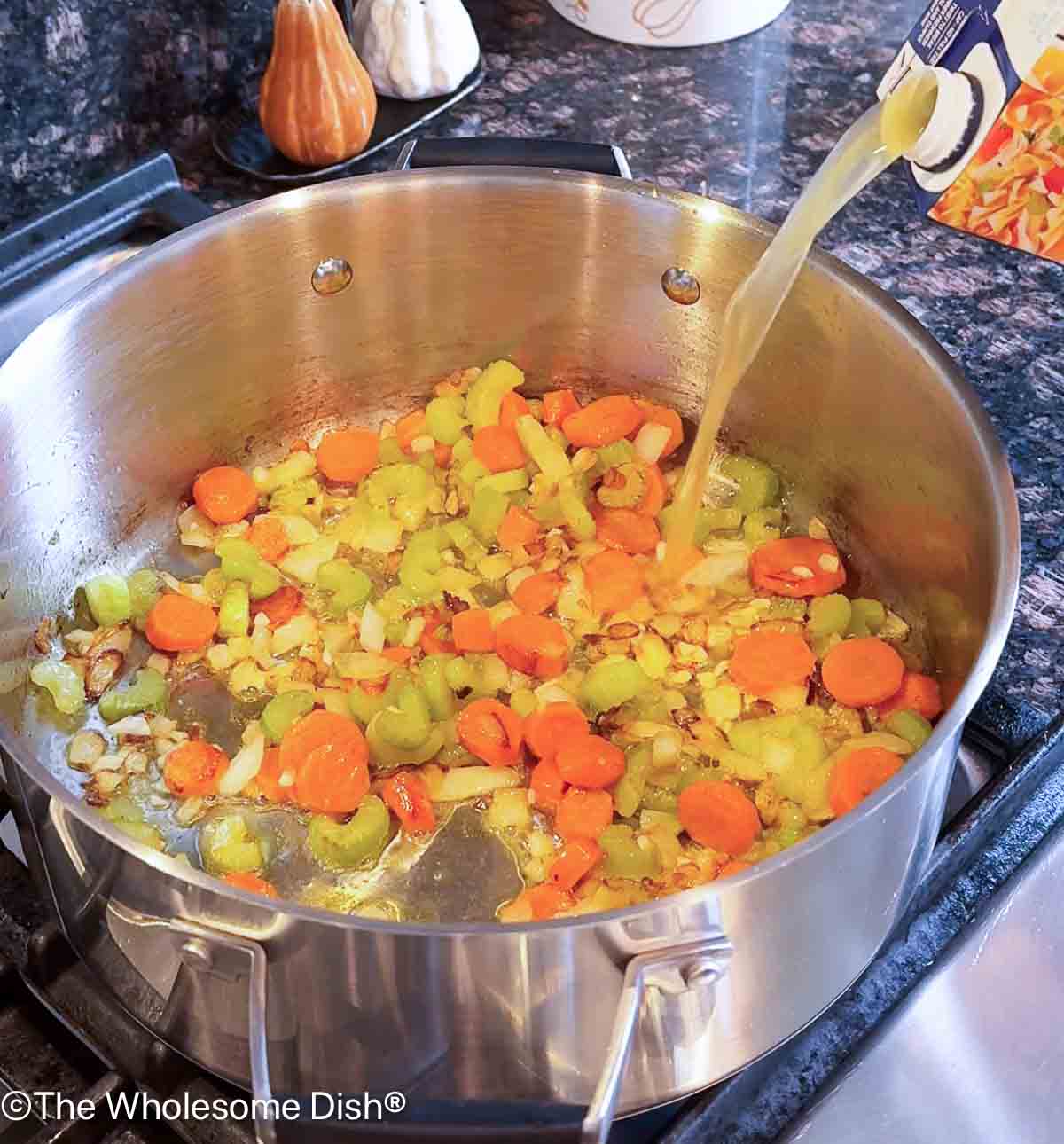 Adding chicken broth to the soup pot.