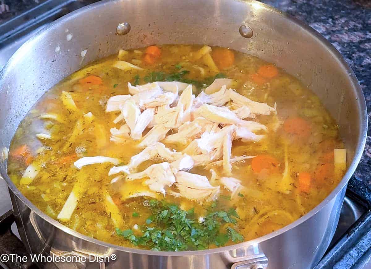 Adding parsley, lemon juice, and pulled rotisserie chicken to the soup pot.