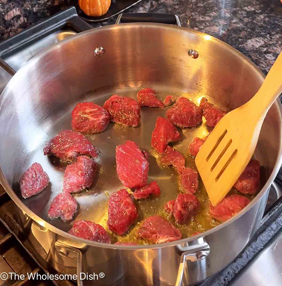 Browning beef stew meat in a soup pot.