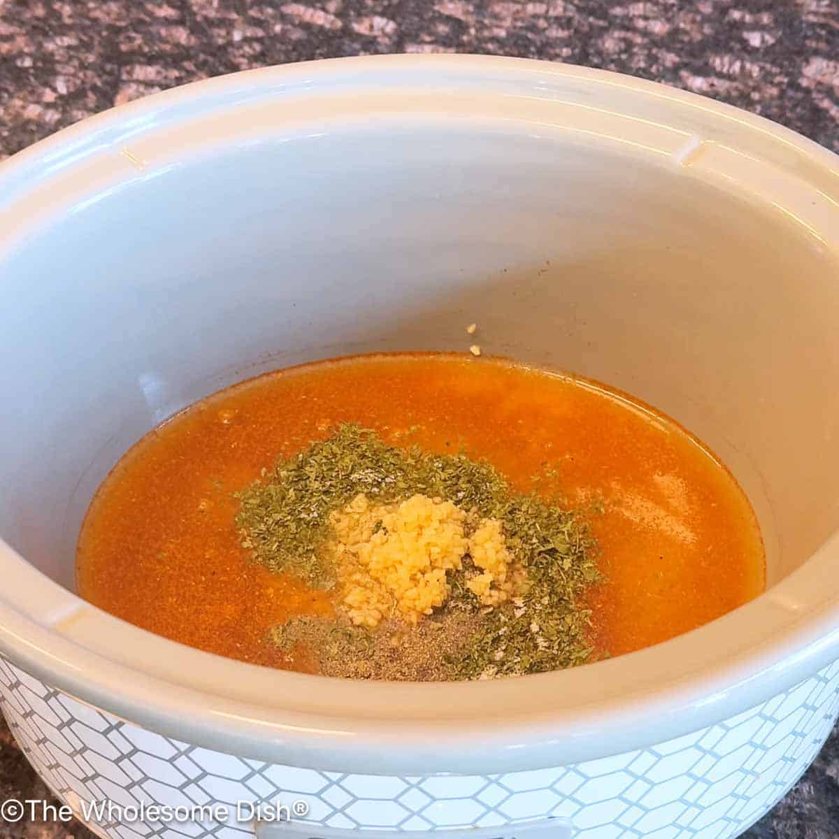 Crock pot full of broth, minced garlic, and seasonings.